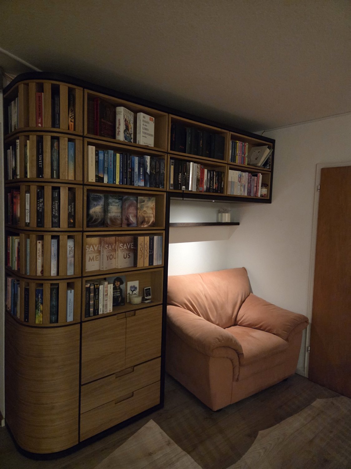 Raumhoher Bücherschrank aus Eiche und Räuchereiche mit gerundeter Stirnseite, eingeräumt mit Büchern, daneben ein Sessel